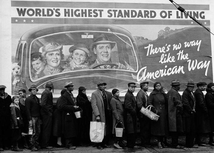 Black and white photo of many people queuing for food in the foreground juxtaposed with a billboard stating 'world's highest standard of living'. juxtaposition examples