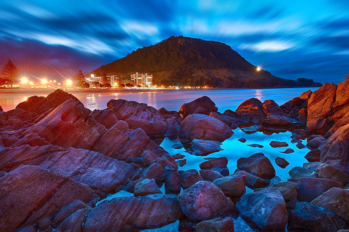 A stunningly colored photograph of a rocky foreground with a mountain and dramatically lit night sky in the background. Using the foreground for landscape photography composition