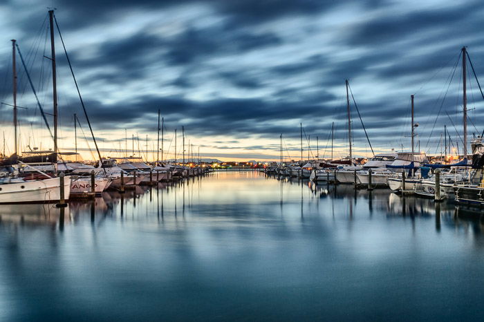 A photo of boats lined up in the harbour beneath a dramatic cloudy sky. Symmetry in landscape photography composition