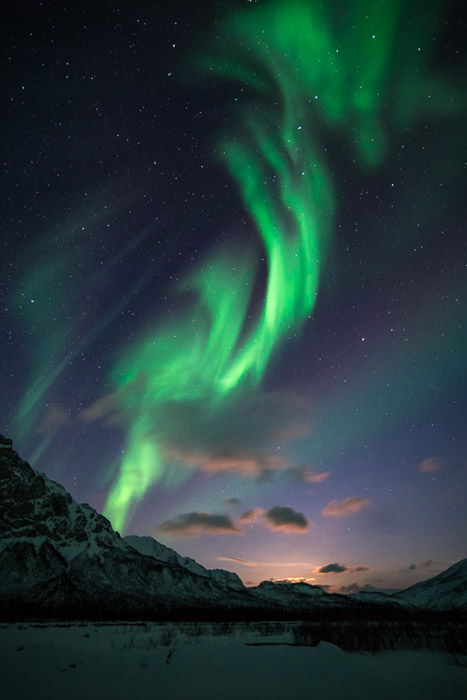 Photograph of the northern lights in Alaska with an icy mountain landscape below. 