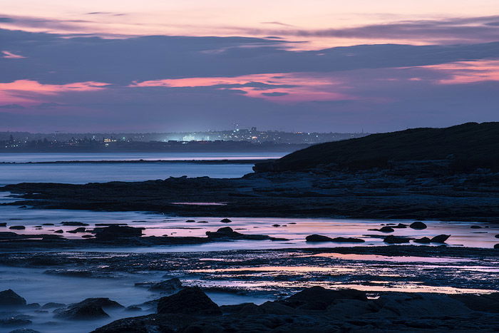 A dramatically lit long exposure seascape with fiery sunset sky.