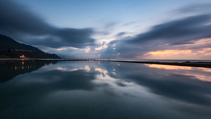 Calm evening seascape with sunset sky and mountains reflected in the sea. 