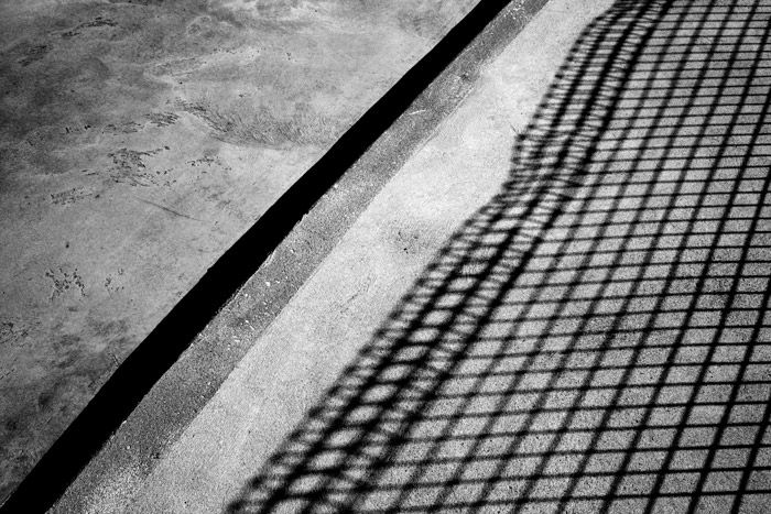 A shadowy black and white photograph of concrete with shadow of a fence, combining light and shadow for abstract photography.