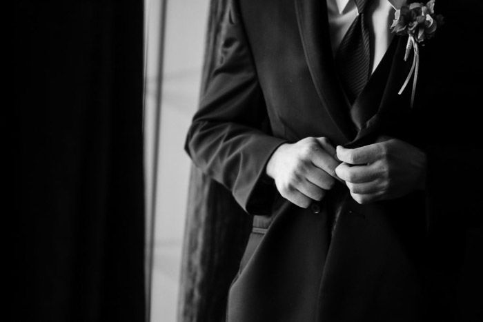 A close up black and white wedding photo of a groom buttoning his jacket