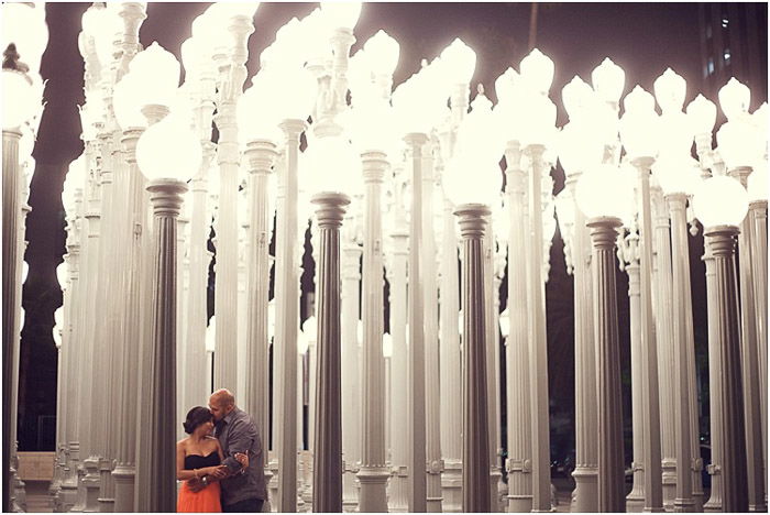 A romantic engagement photography shot of a couple in front of columns of white lamp sculptures