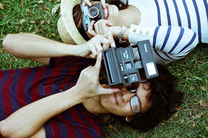 Overhead shot of two people lying on grass, aiming cameras at the photographer. Instagram tips for photography beginners.