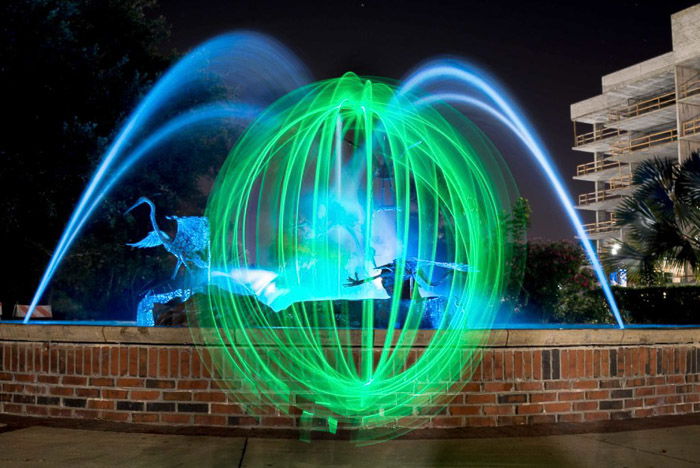 A green light orb in front of a fountain at night.