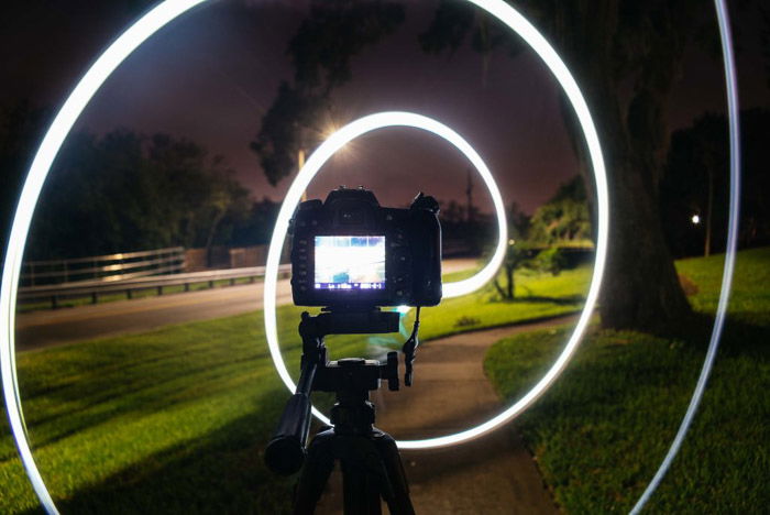 A DSLR camera on a tripod surrounded by a white light spiral