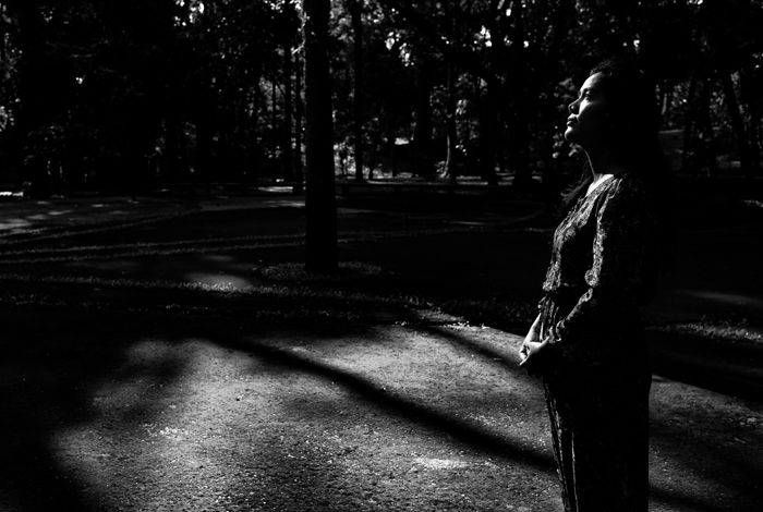 A low key monochrome photography portrait of a girl standing in a dark forest.