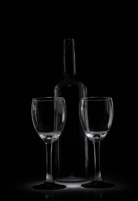 A low key monochrome photography portrait of a wine bottle and two wine glasses