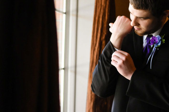 The groom buttoning his sleeves by a window - natural wedding photography lighting