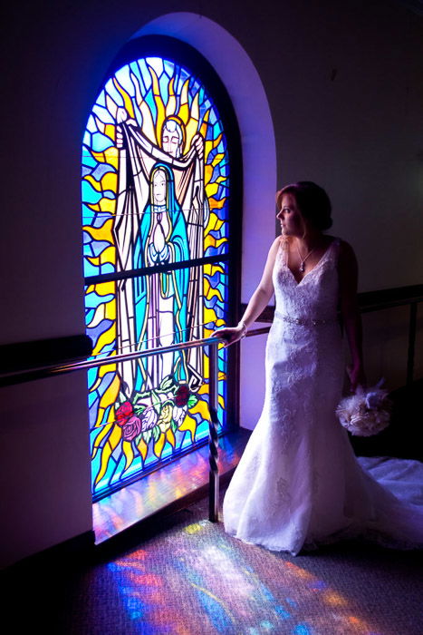 A photo of the bride posing by a large stained glass window - natural wedding photography lights