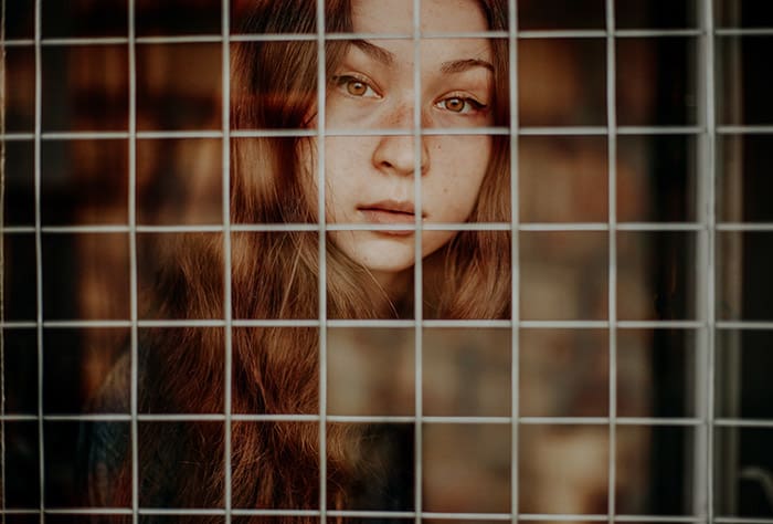 A cut out photo portrait of a brown haired girl behind a chain fence 