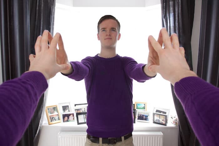 A man in purple jumper touching hands with his reflection in the mirror