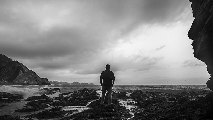 Monochrome coastal photography shot of a man standing on rocks looking towards the ocean using 16:9 aspect ratio