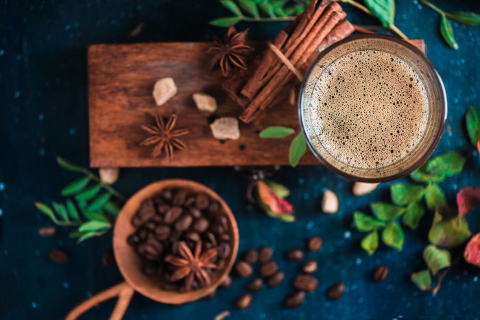 An overhead still live of coffee cups, coffee beans, cinnamon sticks and foliage on a wooden board