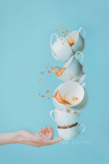 Fun coffee photography shot of six falling cups balanced on the tip of someones finger