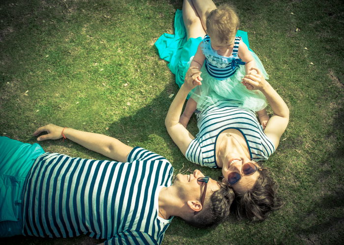 Overhead portrait of a woman holding a small baby and man lying beside her on the grass- composition for family portraits