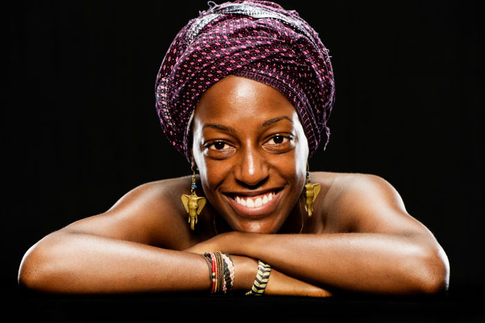 A smiling woman in headscarf scarf poses for portrait against a dark background - how to create a black background for photography portraits.