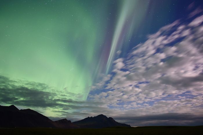 A day-to-night photo of a mountain silhouette and sky with the northern lights and a blue sky with clouds for creative editing ideas