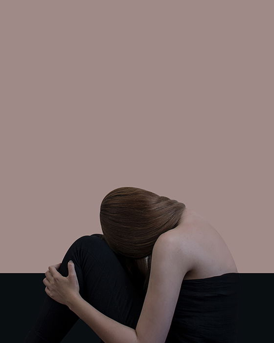 Serene portrait of a girl with head at her knee against a plain background