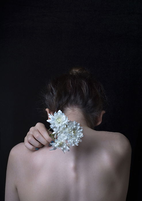 Artistic fine art portrait photography of the back of a female model holding white flowers towards the camera 