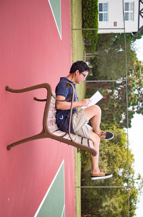 Humourous forced perspective photo of a man taken at angle which makes him look like he is sitting upside down on a bench reading a newspaper