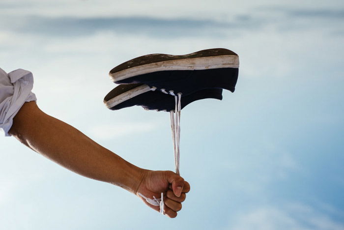 A person holding a pair of shoes by the laces which look like they are floating like a balloon