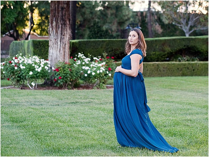 A woman in blue evening dress outdoors posing for a maternity photography session