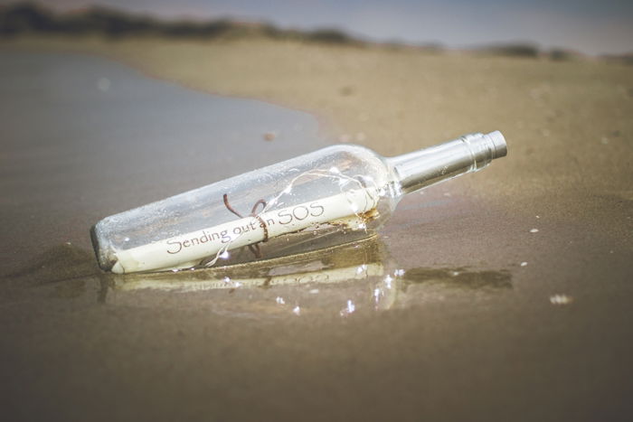 An SOS message inside a bottle in the sand - cool beach photography ideas