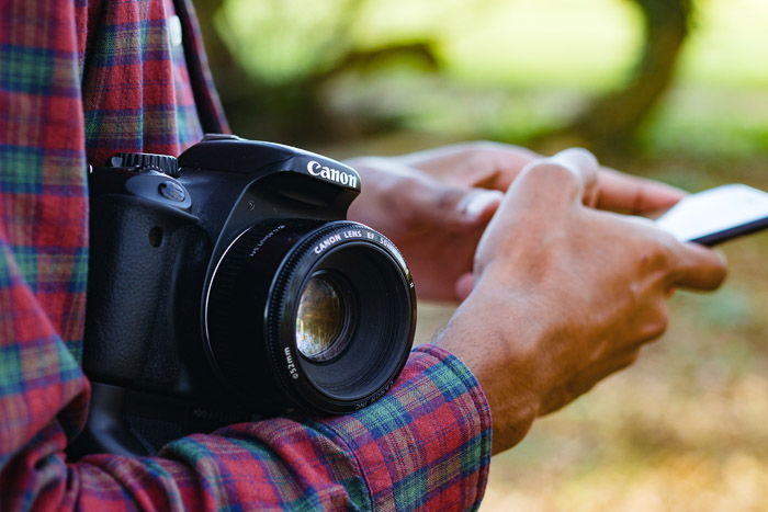 Close up shot of a man holding a DSLR and using his smartphone - why you need photography insurance and camera insurance