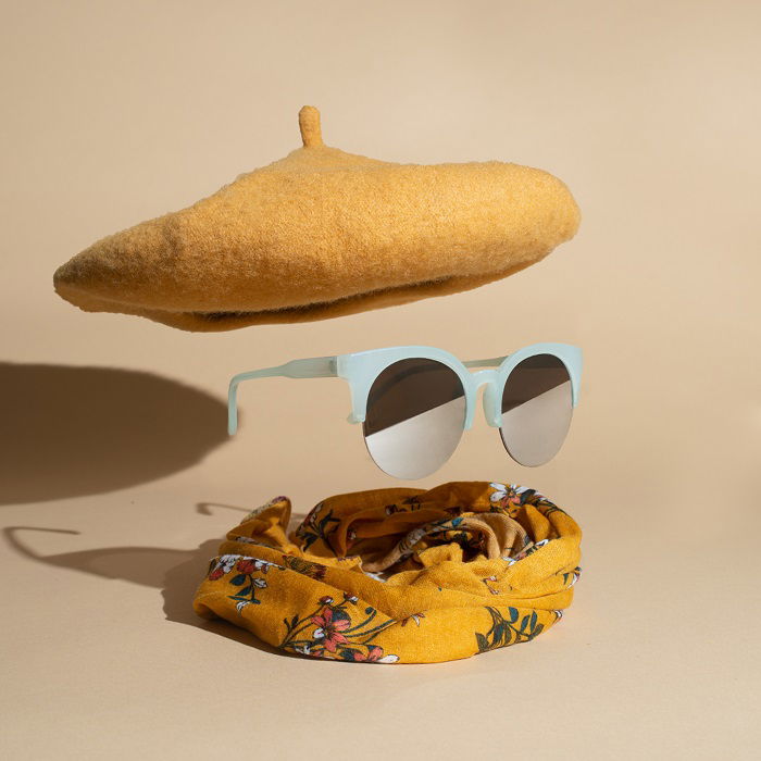 Cool product photography styling example of a levitating pair of sunglasses under a beret and over a scarf