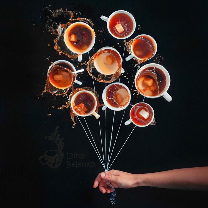 A creative still life flat lay photo idea with 10 cups of coffee arranged in a circle with strings attached and a persons hand holding the strings as if it was a bunch of balloons