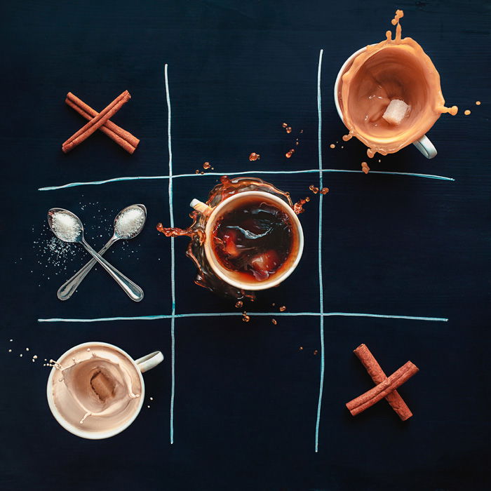 A creative still life photo idea with cups of coffee, cinnamon sticks and spoons arranged in a tic tac toe grid