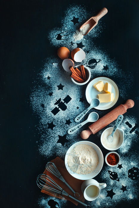 A dark and atmospheric food flat lay still life with flour, eggs, butter and cooking utensils on a dark surface