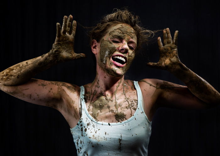 A woman in a white tank top covered in clay