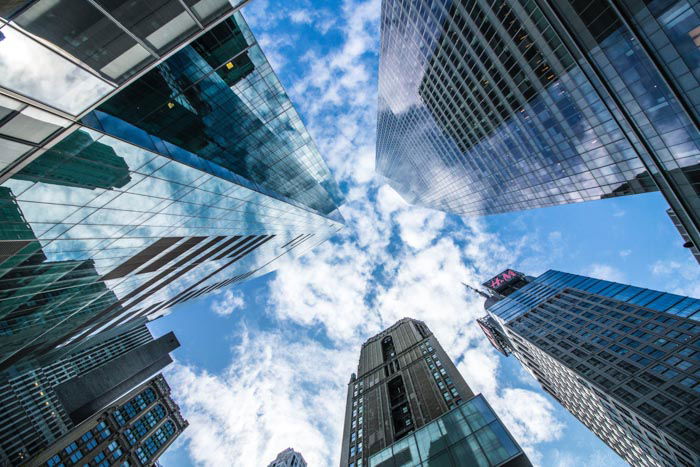 photo looking up at a cloudy blue sky between large skyscrapers