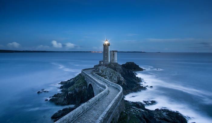 Landscape shot of a stone bridge leading to a lighthouse in low light