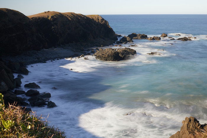 A long-exposure photo of an ocean cover from above with a beach and rock formations