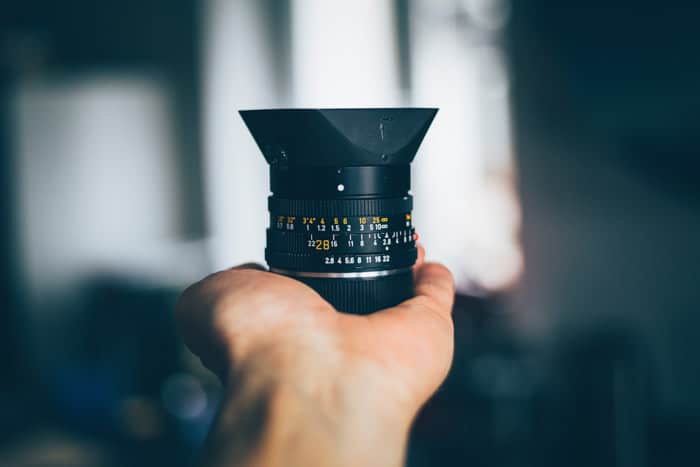 A hand holding a DSLR camera lens with blurry grey background