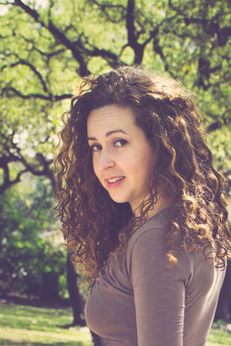 close up of curly haired brunette in a brown dress looking back while walking down a dirt path in a park