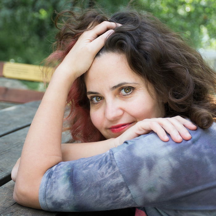 square photo of woman in grey leaning on a wooden picnic table