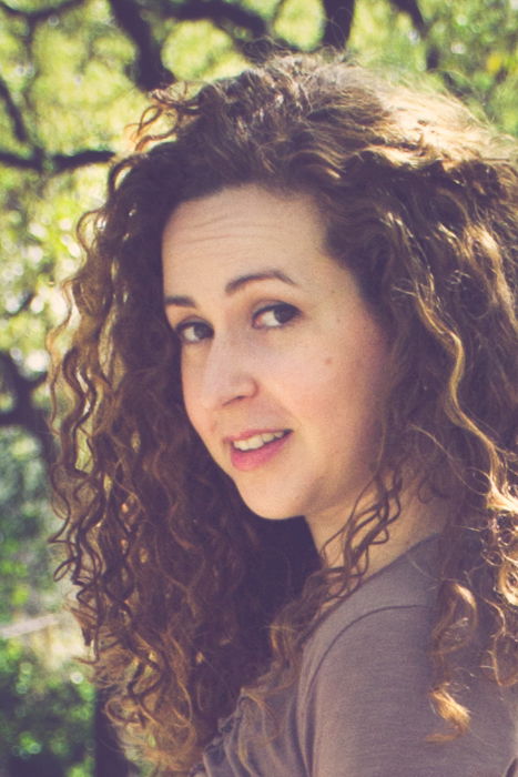 close up head shot of curly haired brunette in a brown dress looking back while walking down a dirt path in a park