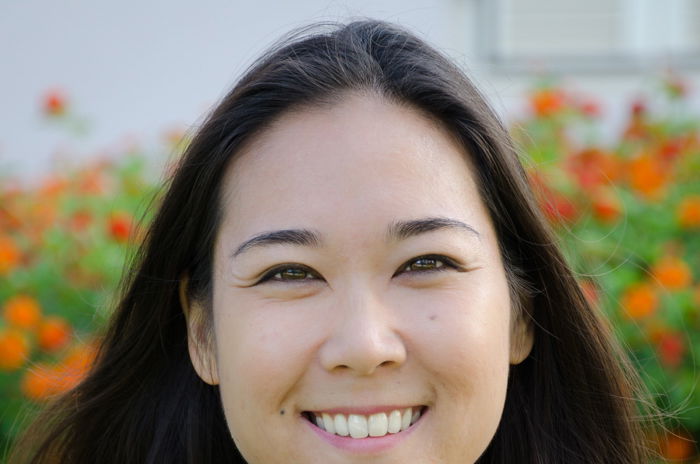 cropped headshot of smiling asian woman in a field of red flowers