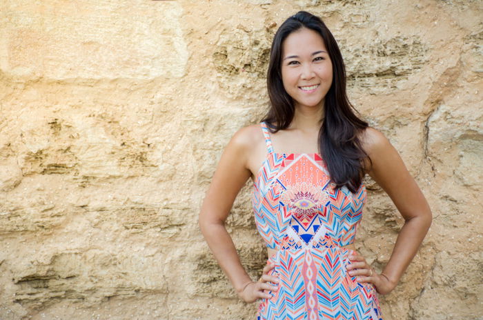 smiling asian woman in pastel geometric patterned dress standing in front of a big stone wall