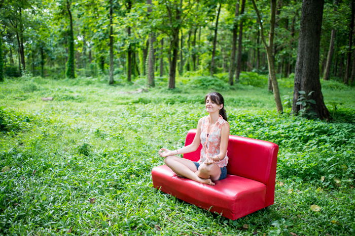 Woman sitting on a red couch in the forest meditating, nice example of editorial portrait photography.