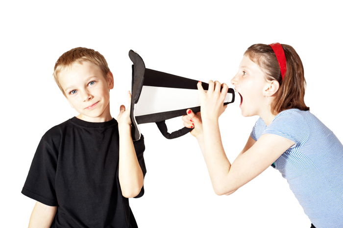 A humourous portrait of a little girl with a megaphone shouts in the boy's ear.