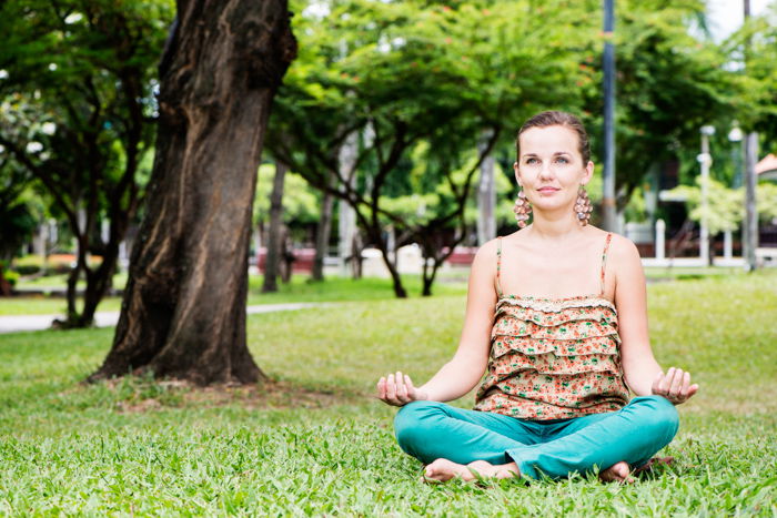 Beautiful young woman in the park sitting crossed legged on the grass.