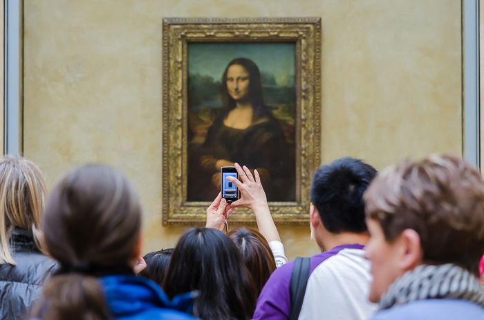 People looking at the Mona Lisa in the Louvre and someone taking a photo on a smartphone