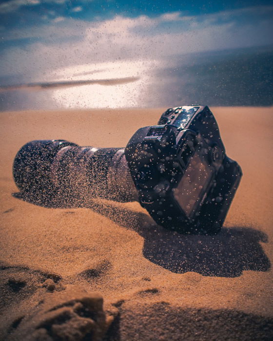 A DSLR camera resting in the sand at the beach